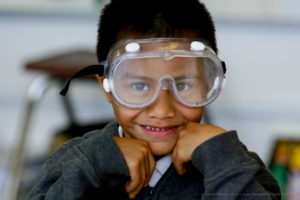 A young student smiles with a pair of clear science goggles over his eyes.