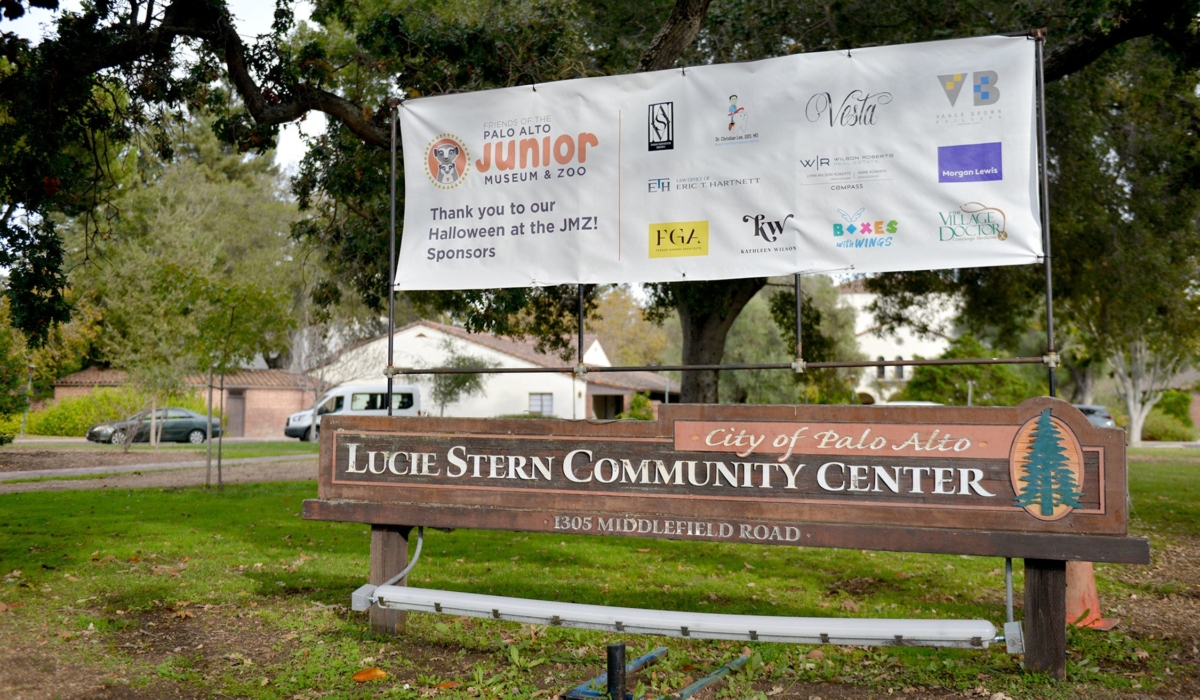 A white sign that reads "Thank you to our Halloween at the JMZ! Sponsors" and features the logos of corporate donors to the event. The sign is hung above the Lucie Stern Community Center brown wood sign.