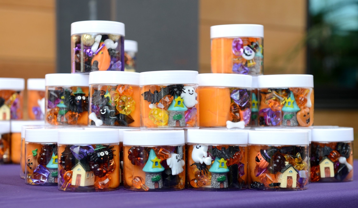 A photo shows small clear jars filled with Halloween goodies, including orange slime, small toy white ghosts, tiny black bats, and black spiders.